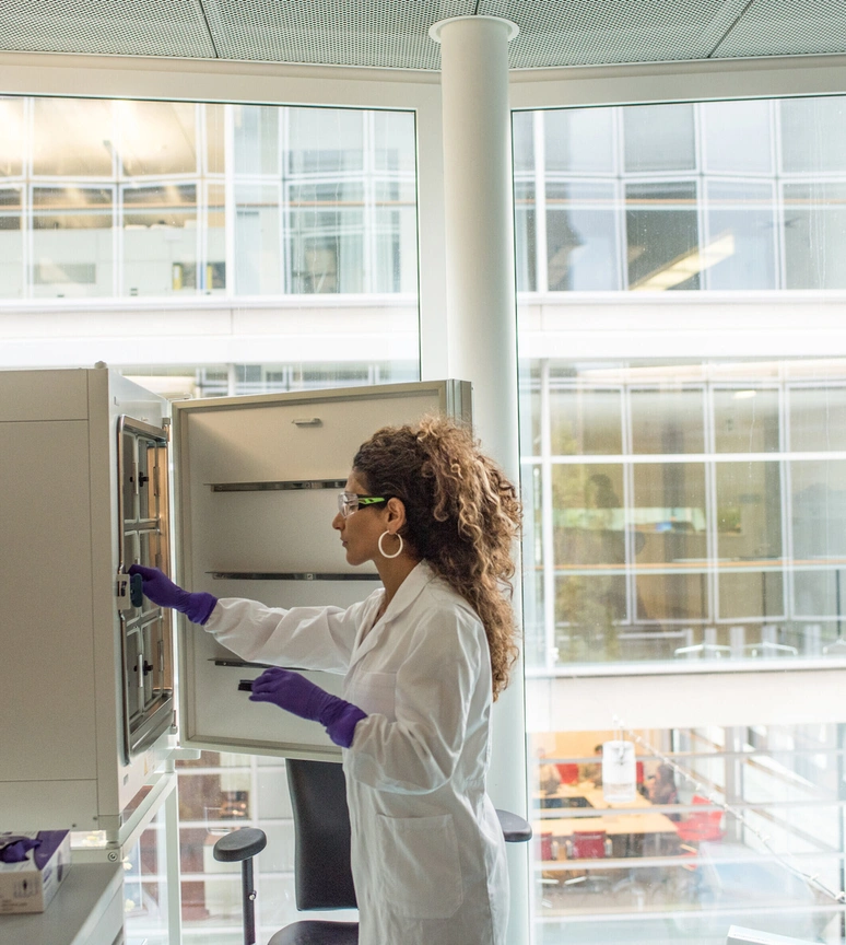 A scientist in a lab coat searching for items in an open cupboard