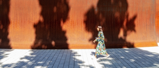 A woman walking past the high walls of the Dirk's Pod structure on campus