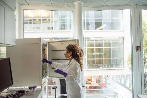 A scientist in a lab coat searching for items in an open cupboard