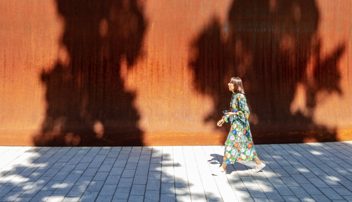 A woman walking past the high walls of the Dirk's Pod structure on campus